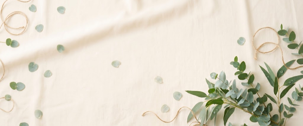 Sprigs of eucalyptus and scattered leaves resting on soft cream linen in natural daylight.